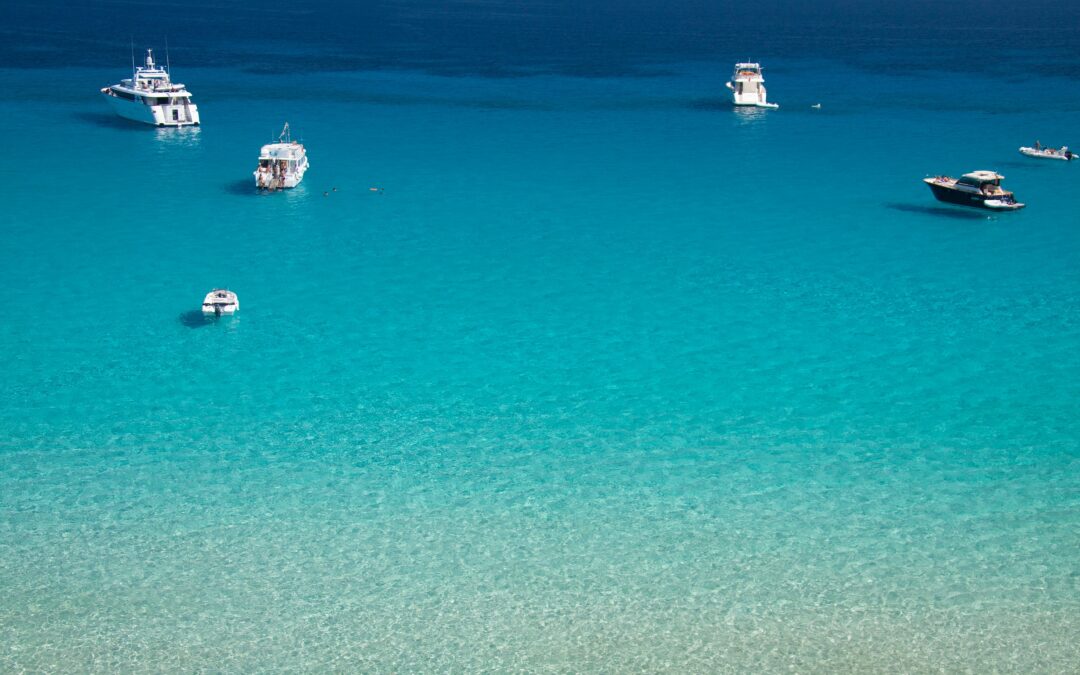 The photo depicts the turquoise waters of Sicily with luxury boats at the horizon