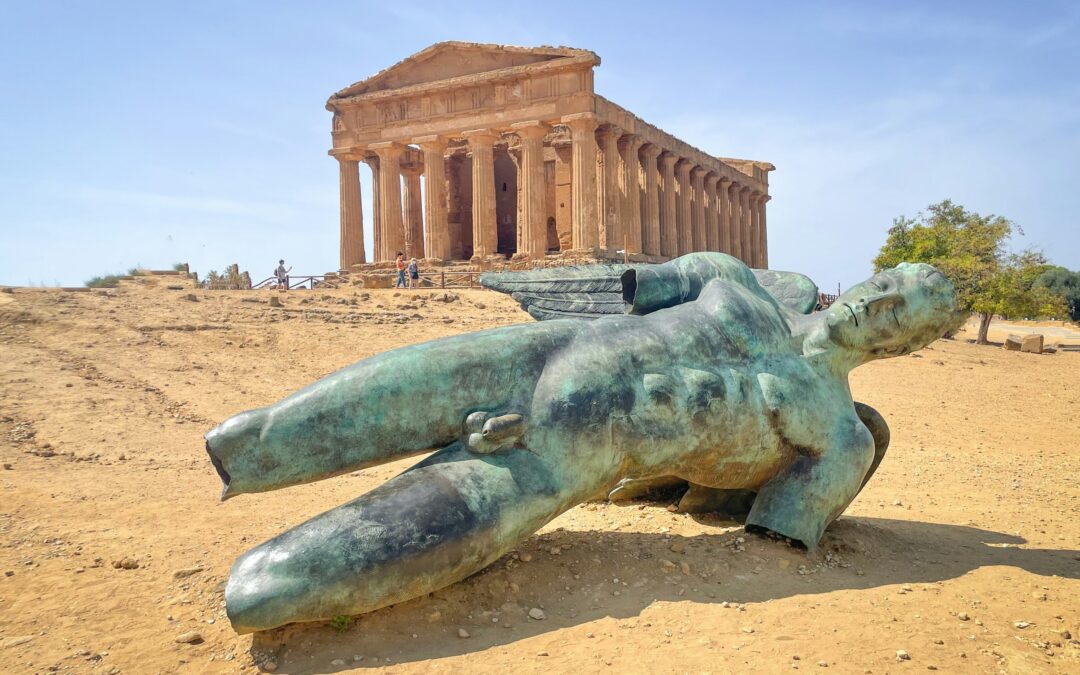 The bronze statue of Fallen Icarus by Igor Mitoraj lying in the foreground, with the Temple of Concordia rising behind it at the Valley of the Temples, Agrigento, Sicily.